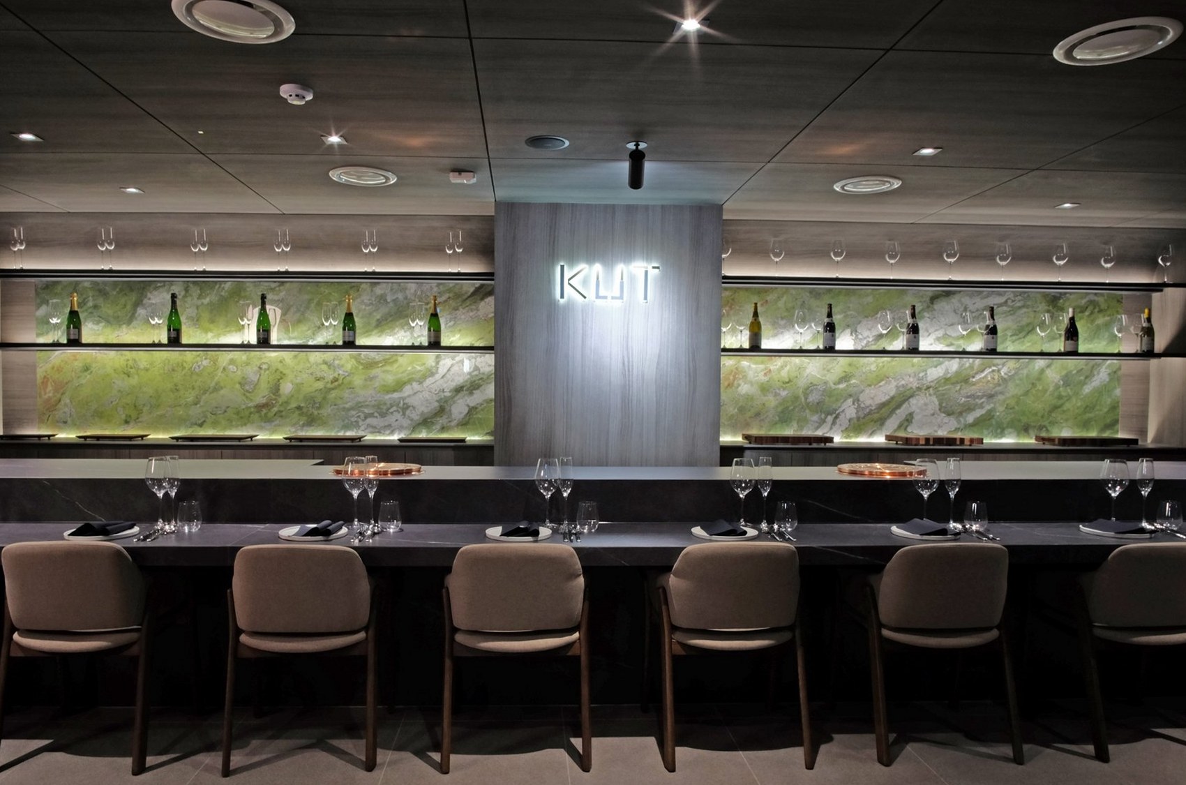 KUT SEOUL's omakase bar counter in Jongno, Seoul — a sleek black-marble chef's counter framed by an illuminated jade-onyx wall and a curated wine display, where the most intimate hanwoo tasting unfolds, course by course.