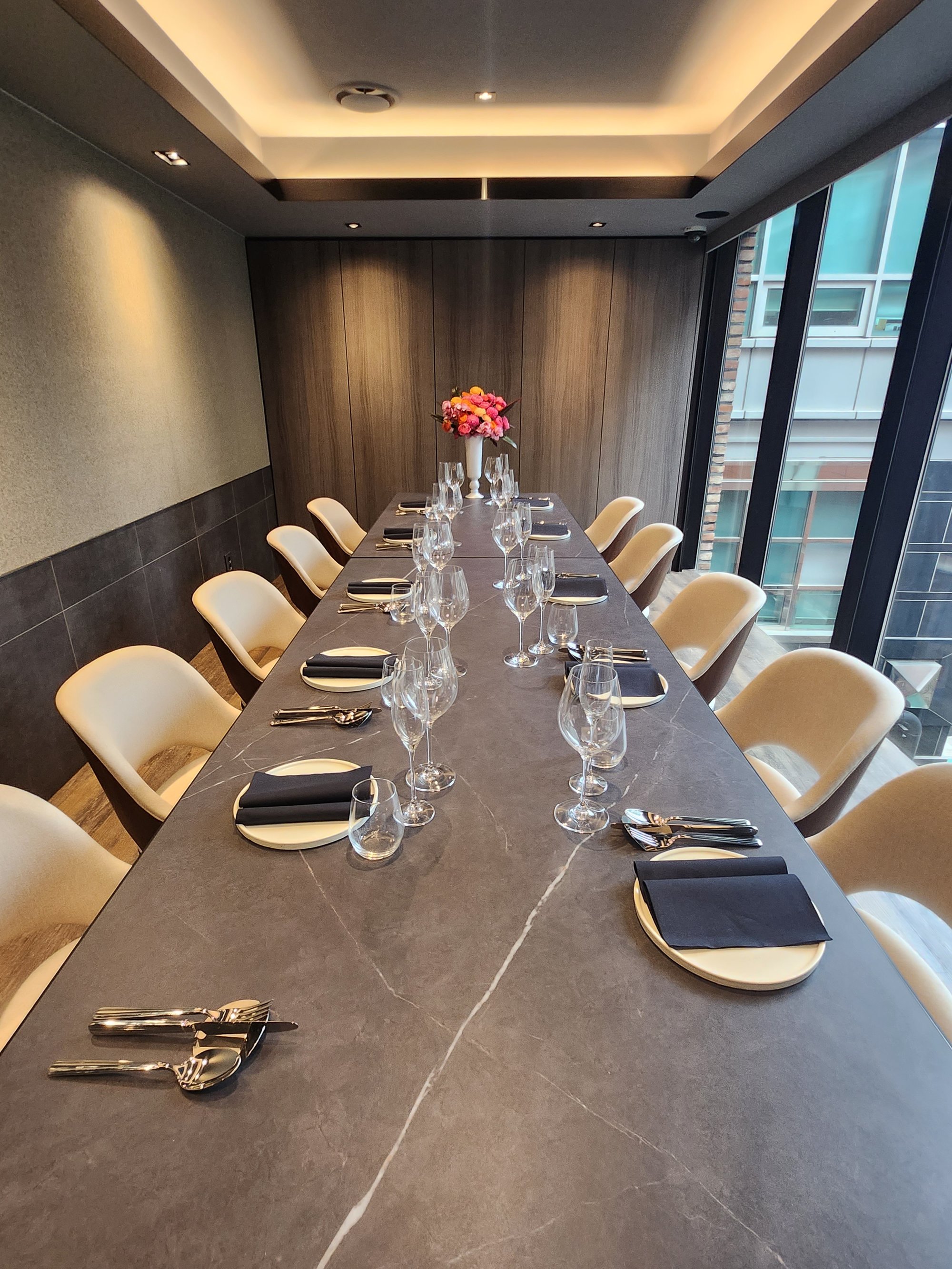 A private dining room at KUT SEOUL — black marble long table set for an intimate hanwoo omakase evening, framed by warm walnut walls and Seoul city light.